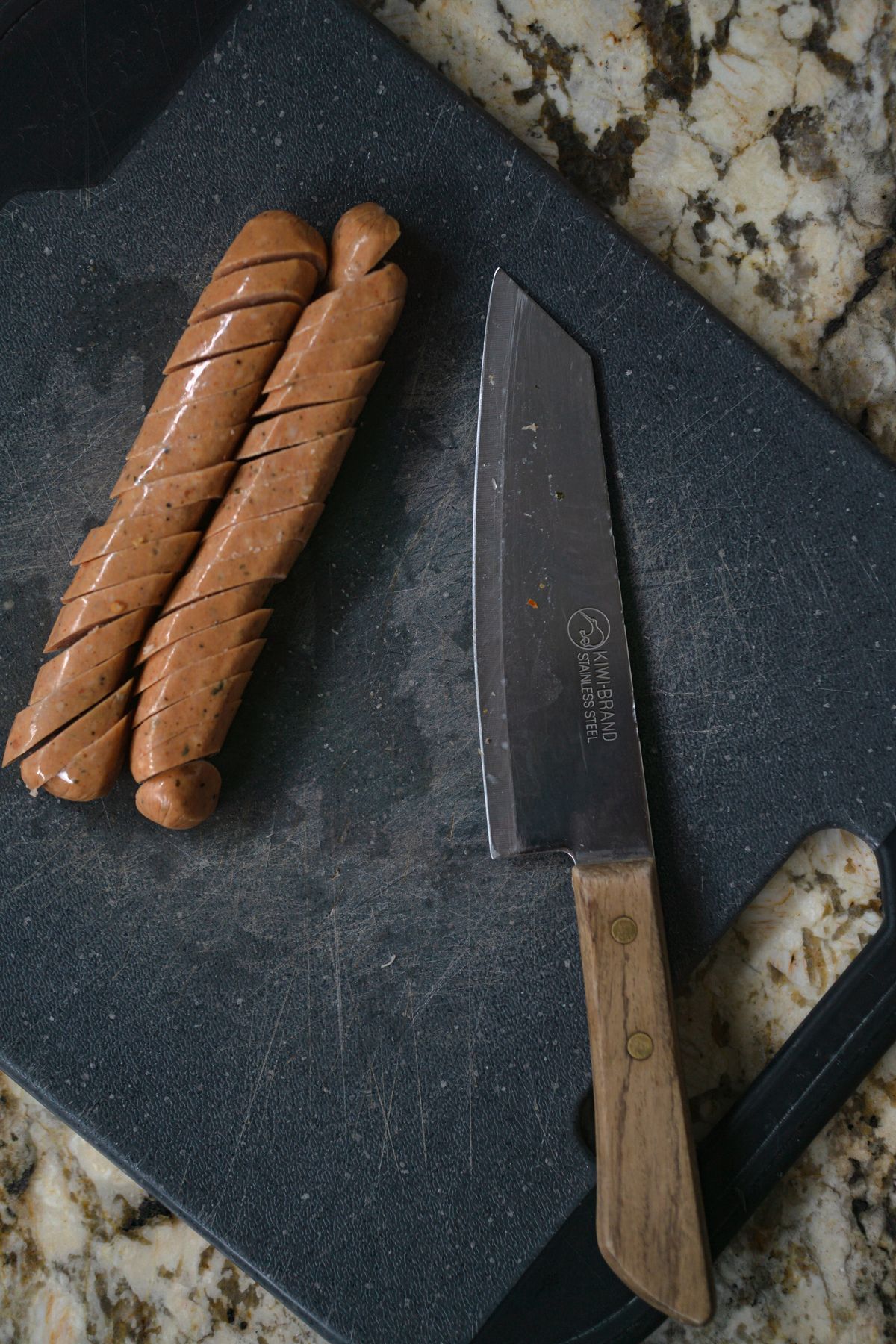 Raw sausages and a knife on a dark stone board